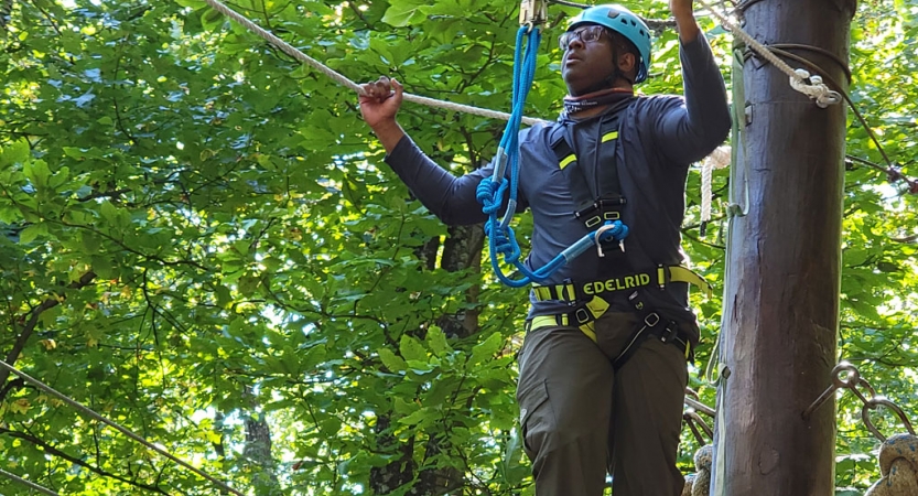 a person wearing rock climbing gear navigates a ropes course